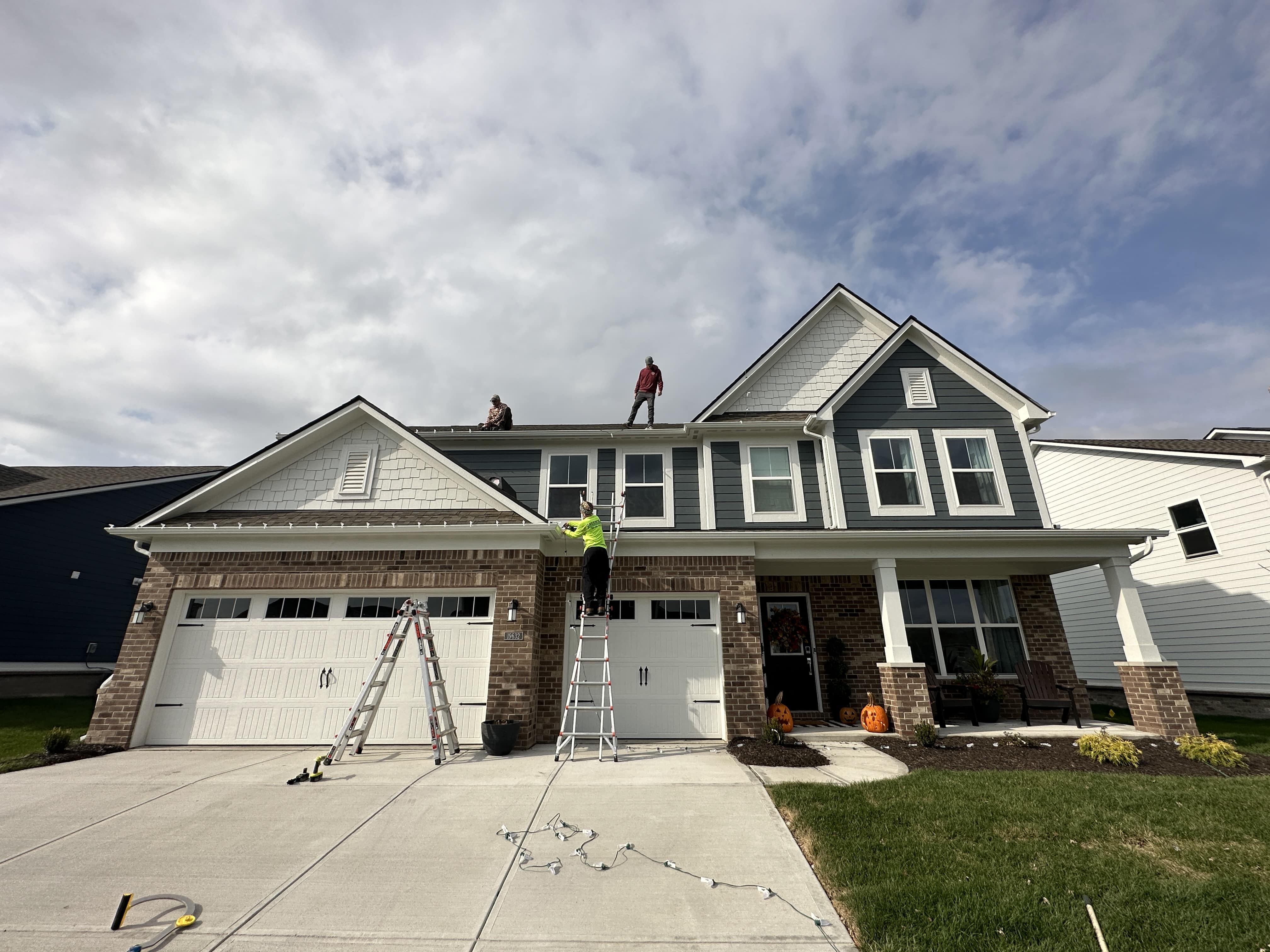 Blue Duck Christmas Lights crew installing Christmas lights on a two-story home in Indianapolis using ladders and safety gear, demonstrating safe roof and ladder practices.